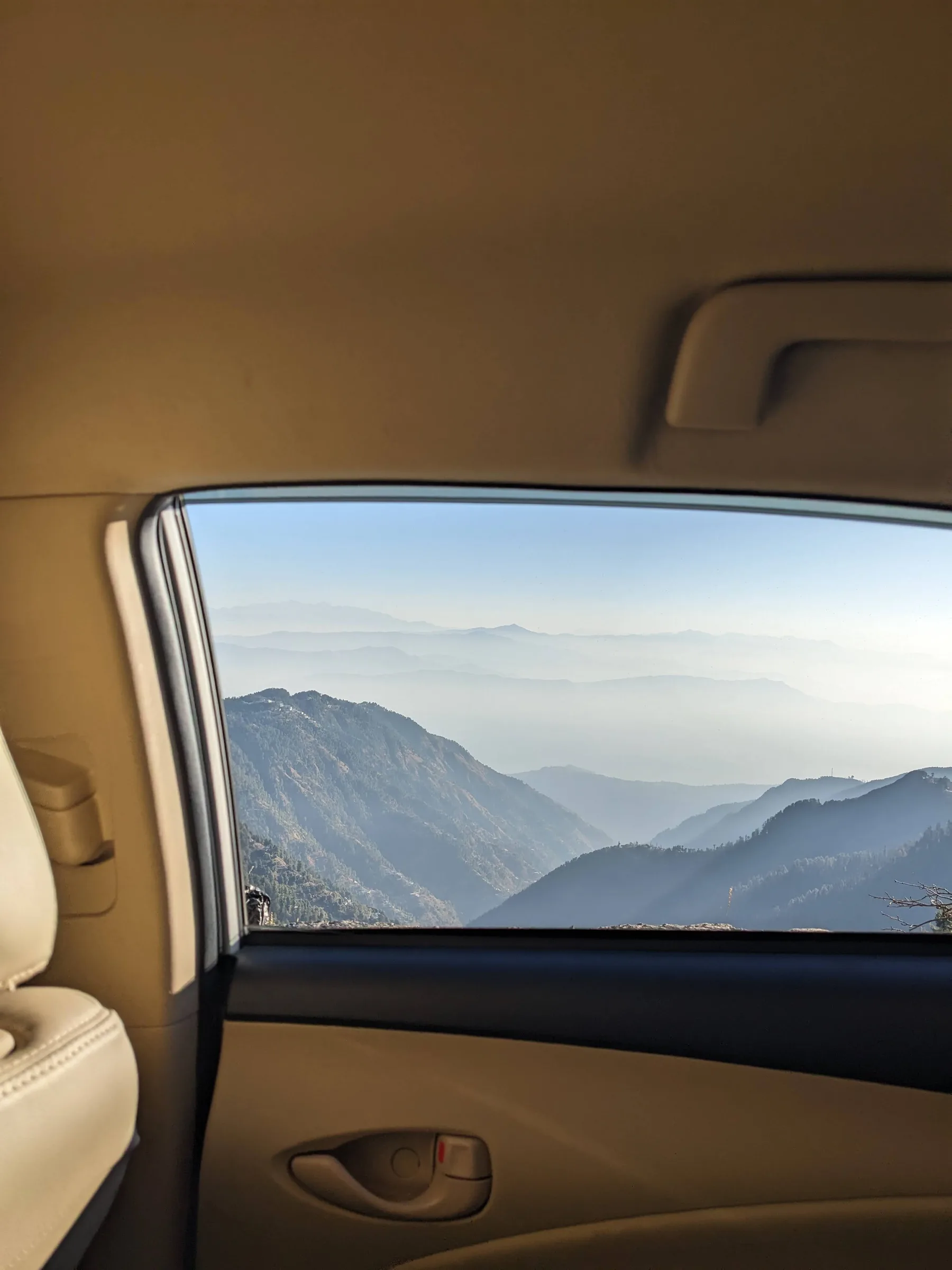Layered blue hills fading into haze, seen through the open rear window of a car.